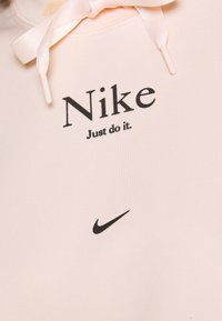 Ljusrosa sweatshirt med svart "Nike"-logotyp och texten "Just do it." Har dragsko med satin-liknande textur och en liten Nike swoosh-emblemet.