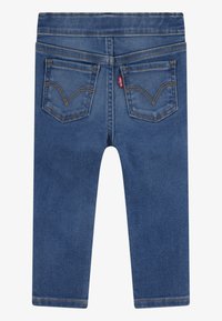 Blauwe denim jeans met een gladde textuur, voorzien van twee achterzakken en oranje stiksels. De tailleband is elastisch voor extra comfort.