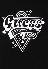 Țesătură neagră cu un design grafic alb, având cuvântul "Guess", anul înființării 1981, un semn de întrebare și accente geometrice.