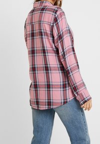 Rosa rutmönstrad skjorta med marinblå och röda accenter, långa ärmar, knäppning vid manchetterna och en avslappnad passform, tillverkad av ett mjukt material.