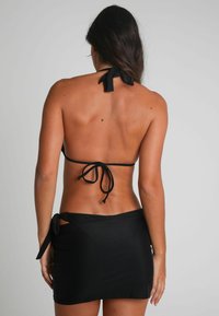 Bikini noir avec des liens derrière le cou et un bas de style jupe assorti. Texture lisse, design minimaliste et forme ajustée.