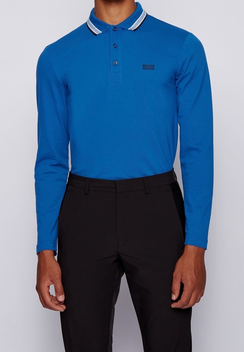 Långärmad pikétröja i klarblå bomull med randig krage, tvåknapps knäppning och en liten svart logotyp på vänster bröst.