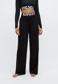 Melnas, brīvi pieguļošas bikses no mīksta auduma, ar elastīgu jostu, regulējamu aukliņu un sānu kabatām.