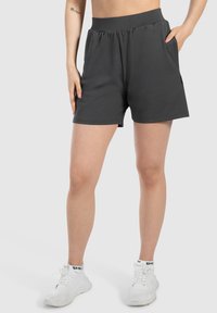 Donkergrijze sportshorts met een elastische tailleband, zijzakken en een gladde, lichte stof. Gekocht met witte sneakers.