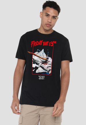 Young man wearing a black t-shirt with "Friday the 13th" text and a graphic of an axe embedded in a blood-stained pillow.