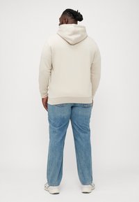Beige sweatshirt met capuchon en een ontspannen pasvorm, gecombineerd met lichtblauwe straight-leg jeans. Zachte textuur, kangoeroezakdetail.