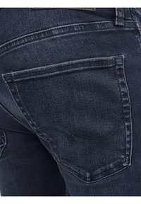 Jeans de mezclilla azul oscuro con un clásico diseño de cinco bolsillos, costuras visibles y un parche de logo de cuero en la cinturilla.