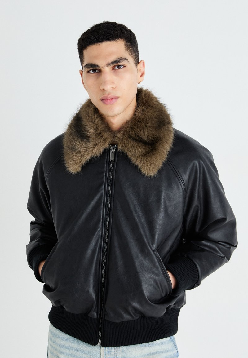 Giubbotto bomber in pelle nera con colletto in pelliccia ecologica marrone, chiusura zip frontale, polsini e vita a costine; texture liscia, vestibilità casual.