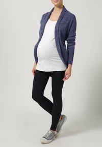 Navy knitted cardigan over a white top, paired with black leggings and gray sneakers. The cardigan has an open front and long sleeves.