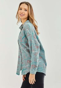 Light blue button-up shirt with a textured finish, featuring multicolored abstract doodles and a relaxed fit. Long sleeves and button cuffs.