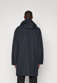 Manteau sombre, imperméable, avec une capuche, présentant un design simple et une coupe décontractée. Texture lisse ; sans motifs ni accents visibles.