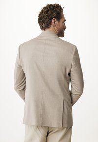 Světlý béžový blazer s úzkým střihem, strukturovanými rameny a jemnou texturou; má jeden větrací otvor na zádech a klopové límce.