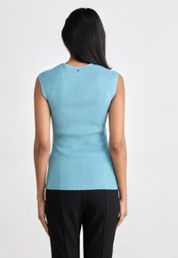 Top senza maniche di colore blu chiaro a coste, con scollatura tonda e un piccolo bottone decorativo sul retro, abbinato a pantaloni neri.