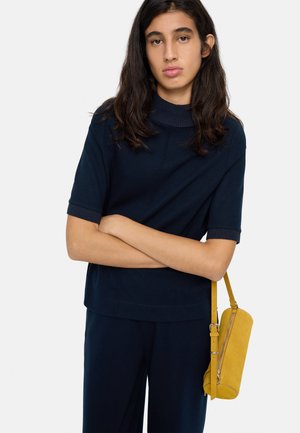 Granatowy top z krótkim rękawem z żebrowanym półgolfem; zestawiony z ciemnymi spodniami i cylindryczną torebką ze żółtej zamszowej skóry na ramię.