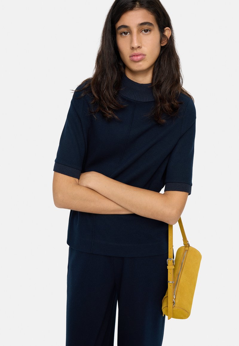 Granatowy top z krótkim rękawem z żebrowanym półgolfem; zestawiony z ciemnymi spodniami i cylindryczną torebką ze żółtej zamszowej skóry na ramię.