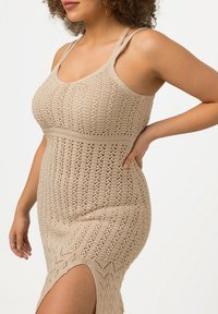 Mjukt bodycon klänning i beige med ett texturerat mönster, med tunna axelremmar och en hög sidoklyvning för extra detalj.