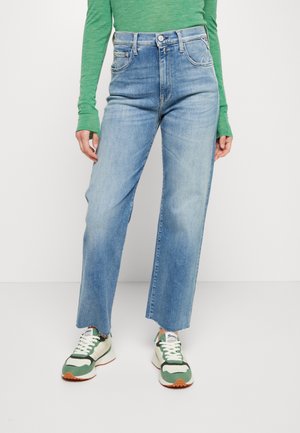 Vaalean siniset farkut suoran lahkeen muotoilulla, joissa on korkea vyötärö, repaleinen helma ja hienovaraiset takataskujen yksityiskohdat. Yhdistettyinä vihreisiin tennareihin.