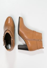 Une paire de bottines en cuir beige avec fermeture éclair sur le côté et talons blocs, présentées en vue de dessus et de côté sur un fond blanc.