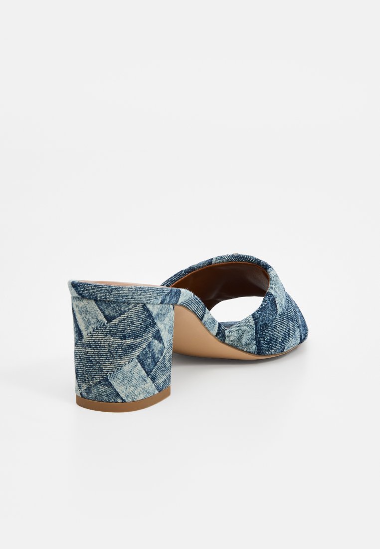 Tacón de denim azul tejido con forma cuadrada, parte trasera abierta y suela suave color tostado. Presenta un patrón de tejido en cesta texturizado en el exterior.