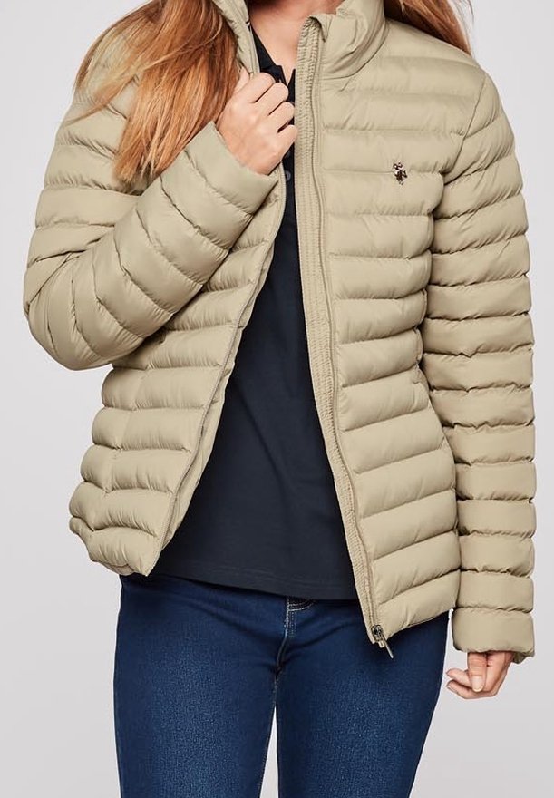 Beige puffer jacket with horizontal quilted design, high collar, and zip closure. Features a small logo on the upper left side.