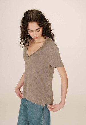 Haut à col V, à manches courtes, en tissu léger et brillant, avec des fentes sur les côtés et une coupe décontractée, associé à un jean bleu.