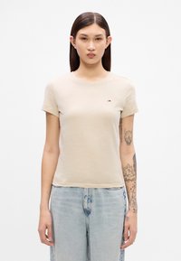 Beige tettskjorte med rund hals, korte ermer og en liten brodert logo på brystet. Mykt bomullsmateriale.