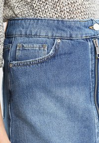 Vaaleansiniset farkut, joissa on vetoketjusuljenta, etutasku ja hillitty kulutus. Kangas on pehmeä ja klassinen istuvuus.