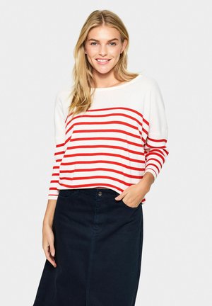 Witte trui met rode horizontale strepen, ronde halslijn en driekwart mouwen, gecombineerd met een donkerblauwe denim rok.