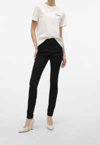 Biały bawełniany t-shirt z niebieskim napisem "City Lights", w połączeniu z czarnymi obcisłymi dżinsami i beżowymi koturnami. Prostota wzoru i dopasowany krój.