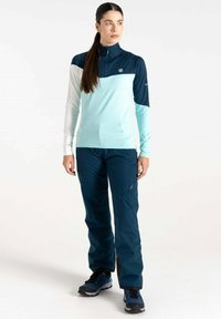 Hellblaues und dunkelblaues Langarmoberteil mit einem Reißverschluss am Hals, kombiniert mit dunklen navy Hosen mit Seitentaschen und taillierter Passform, getragen mit Wanderschuhen.