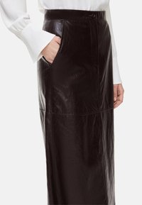 Gonna in pelle nera con vita alta, tasche frontali e design elegante con texture liscia e forma strutturata.