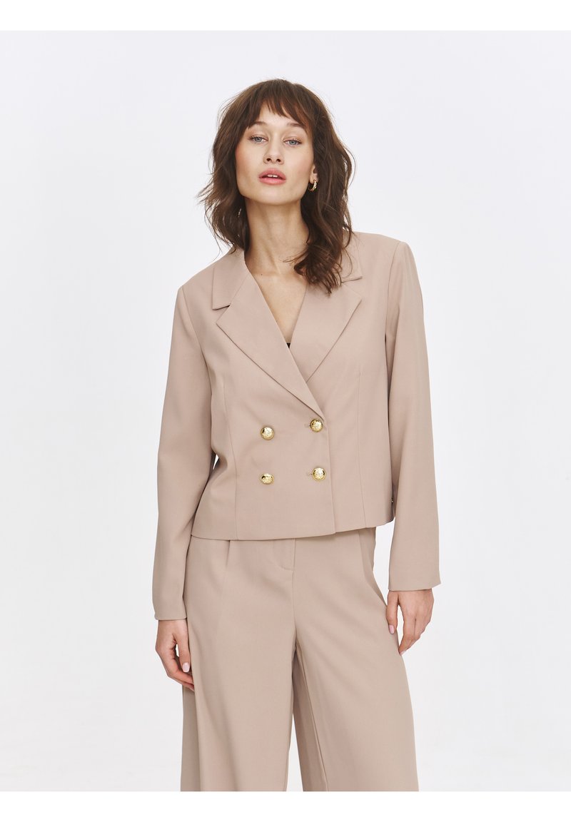 Beige double-breasted blazer with gold button accents, long sleeves, and a cropped fit, paired with matching tailored pants. Smooth texture.