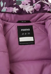 Paarse geïsoleerde jas binnenin met bloemenpatroon op de capuchon, maatlabel en een label met de tekst "Duurzaam ontwerp uit Finland" in witte letters.