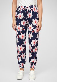 Pantaloni jogger floreali navy con grandi fiori bianchi e rosa, vita elastica e polsini, e coulisse regolabile. Abbinati a scarpe bianche.