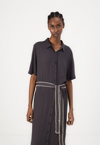 Robe gris foncé à manches courtes, devant boutonné, col et détail de ceinture tressée en couleur contrastante. Tissu texturé.