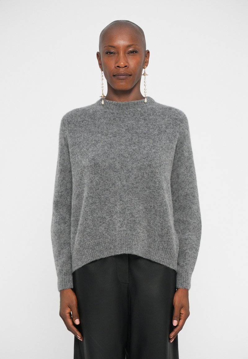 Maglione grigio a maglia con un collo alto, morbido al tatto e orlo a coste. Abbinato a pantaloni in pelle nera, con maniche a goccia ben evidenti.