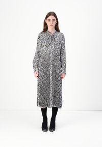 Schwarz-weiß gemustertes Kleid mit einem Kragen, langen Ärmeln und einer taillierten Taille, kombiniert mit schwarzen Stiefeln und knielangen Socken.