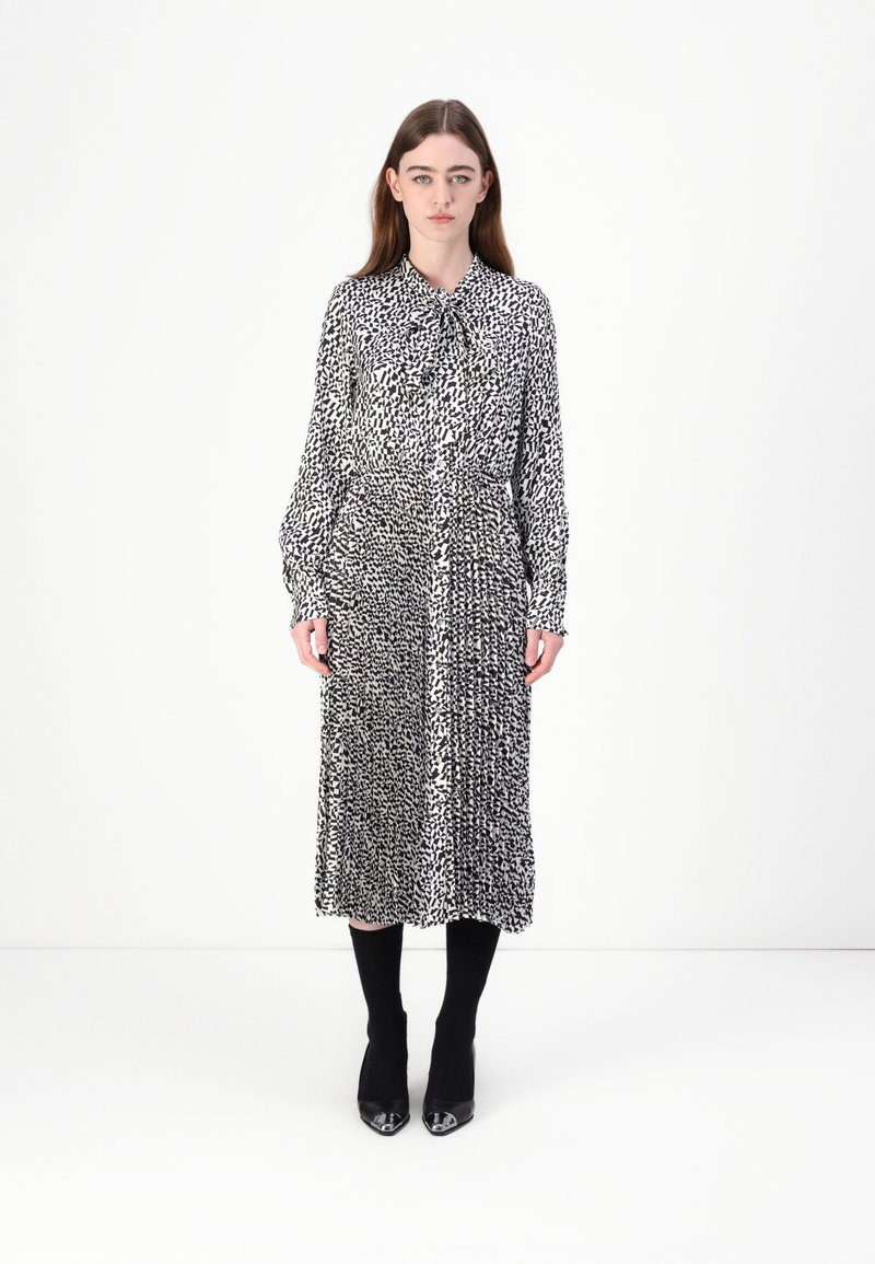 Schwarz-weiß gemustertes Kleid mit einem Kragen, langen Ärmeln und einer taillierten Taille, kombiniert mit schwarzen Stiefeln und knielangen Socken.