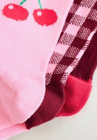 Färgglada strumpor med en rosa bakgrund och körsbärsmotiv, texturerad tyg och en blandning av röda och bordeaux-rutiga mönster.