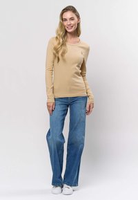 Beige ribbad långärmad topp med rund halsringning, kombinerad med ljusblå utsvängda jeans och vita sneakers. Enkel design utan mönster.