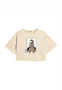 Camiseta corta beige de algodón, con un estampado gráfico de un peinado de chica con un lazo de estampado de leopardo y acentos de texto.