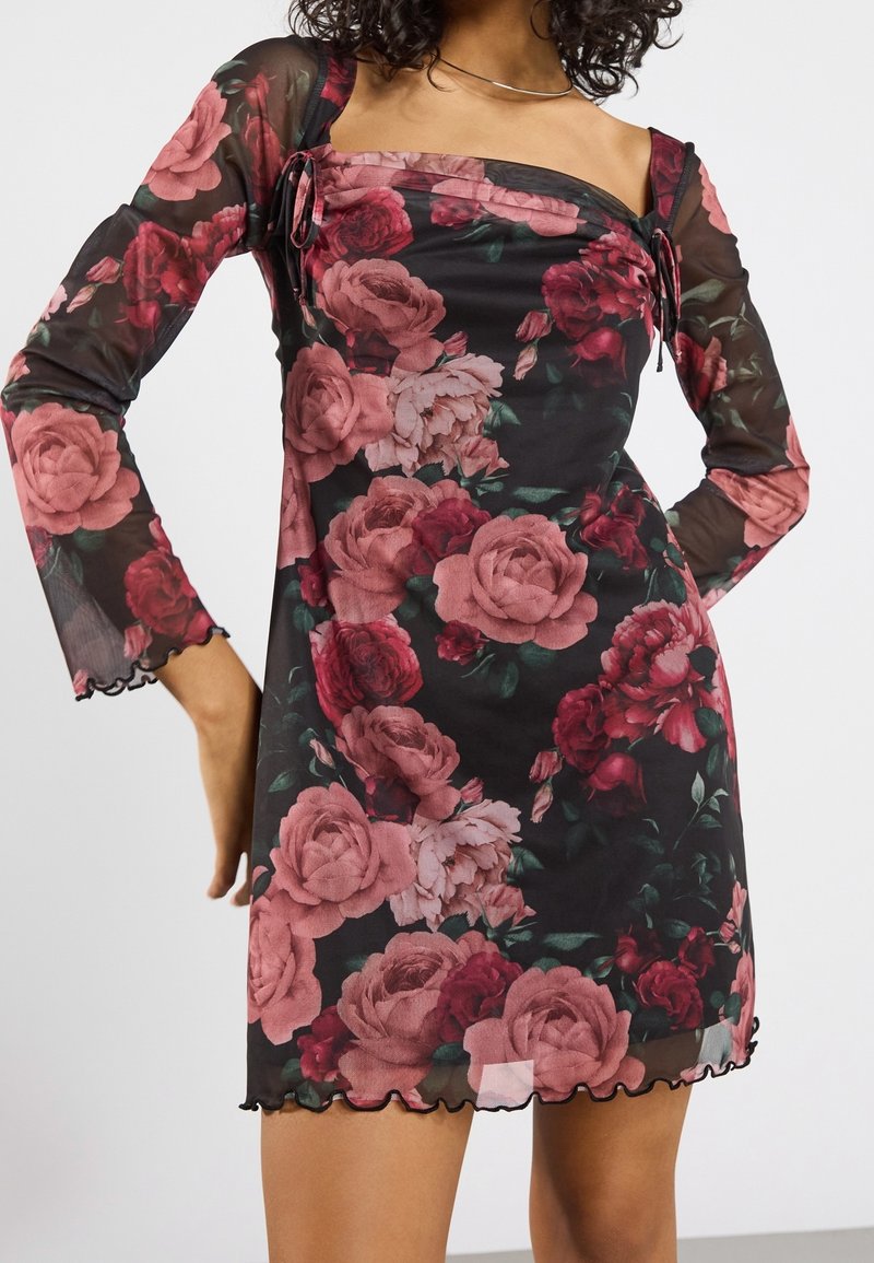 Mini-robe noire transparente à manches longues avec motif de roses roses et rouges, encolure carrée et délicate bordure à volants aux manches et à l'ourlet.