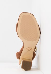 Sandale en daim marron à bout ouvert avec talon bloc, visible depuis la semelle, avec une semelle crantée et une taille 8M avec logo de la marque.