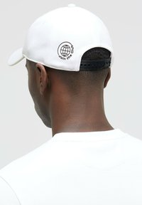 White baseball cap with a curved bill and adjustable black strap. Embroidered design on the back features a globe and the text "Join the Club."