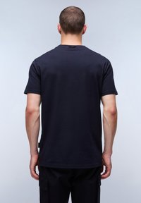 Černé bavlněné tričko s krátkým rukávem, kulatým výstřihem a decentní etiketou na levé straně blízko lemu. Hladká textura a ležérní střih.