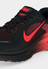Μαύρο και κόκκινο παπούτσι τρεξίματος Nike Air Zoom Vomero 18 με φωτεινό κόκκινο λογότυπο Swoosh και ετικέτα "RUN" στη γλώσσα, που δείχνει πλευρικές και επάνω λεπτομέρειες.