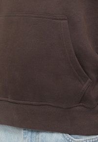 Brun bomulds sweatshirt med frontlomme, ribbet nederkant og glat tekstur, parret med lys blå denim.