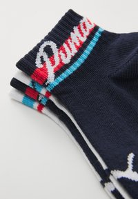 Trois paires de chaussettes à mi-mollet en marine, blanc et gris. Chacune a un revers côtelé avec le logo "Puma" en rouge et blanc, rehaussé de rayures bleues.