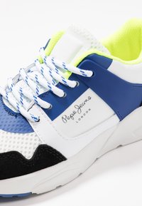Sneaker blu, bianco e nero con tomaia in mesh, collare imbottito e dettagli in giallo neon. Presenta una suola testurizzata e lacci blu.