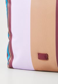 Multicolored cushion featuring wide stripes in purple, brown, and teal with a textured finish and a small maroon tag detail.